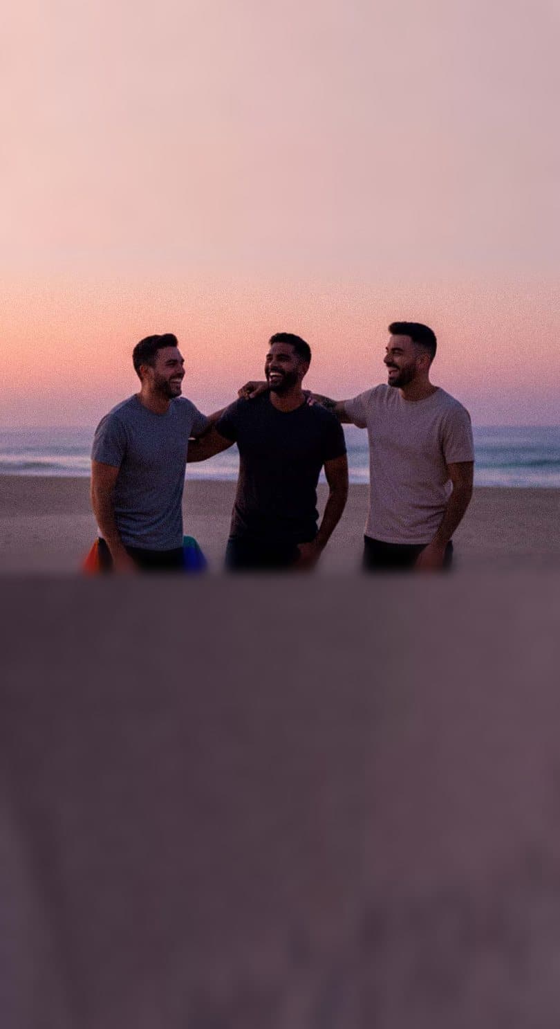 Homens gays sorrindo na praia ao pôr do sol