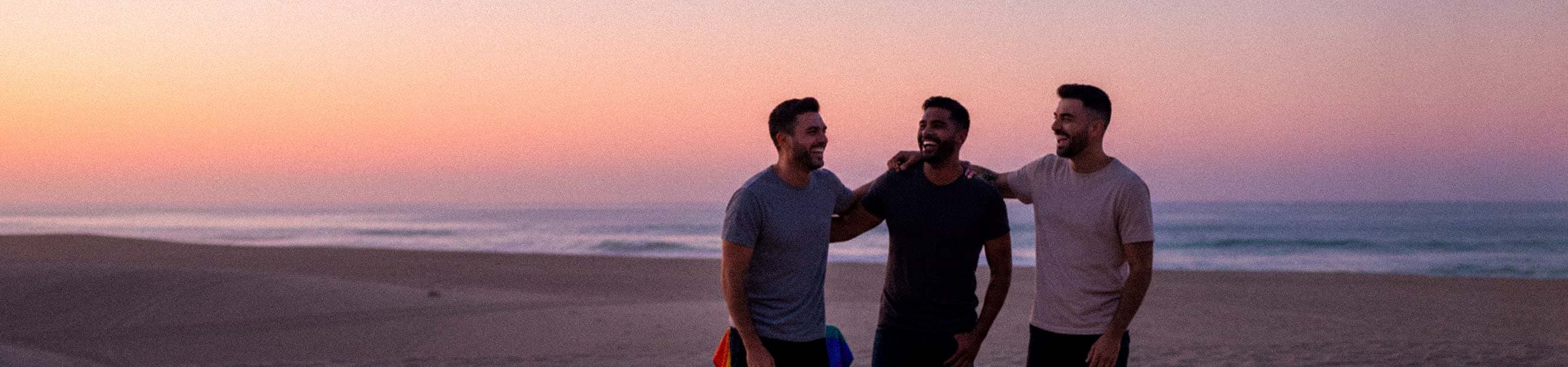 Homens gays sorrindo na praia ao pôr do sol